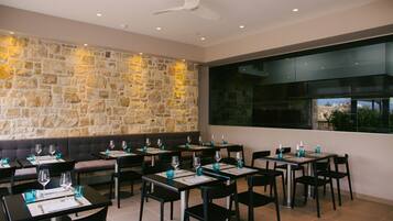 A restaurant with stone walls, black chairs, and tables set with wine glasses and menus.