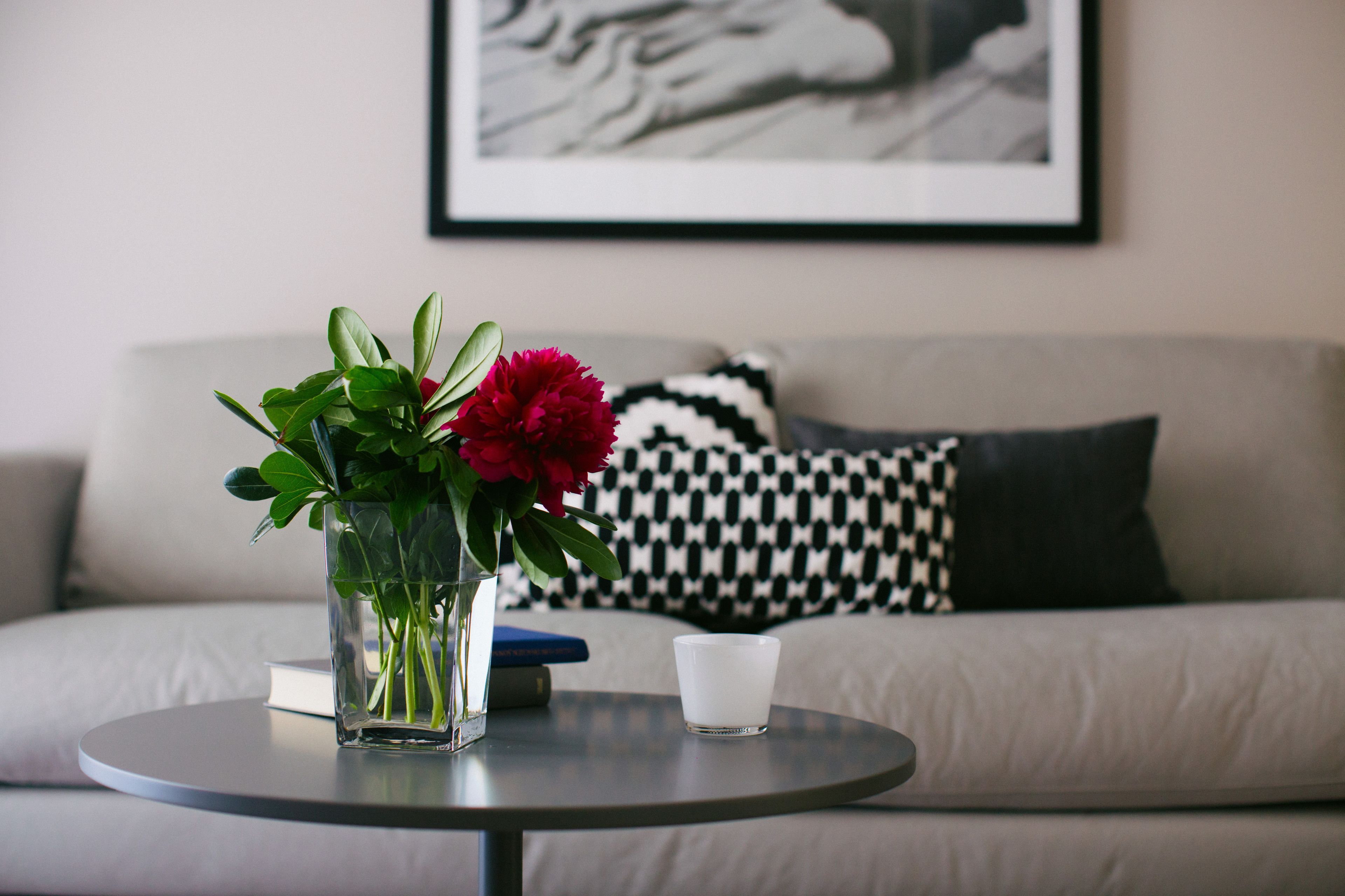 A round table with a vase of flowers and a glass of water on a sofa with patterned pillows.