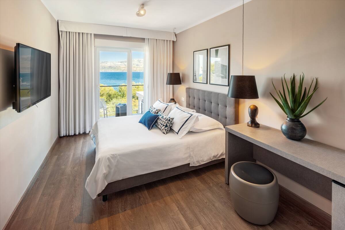 Una habitación de hotel moderna con cama, escritorio, televisor y vista al mar.