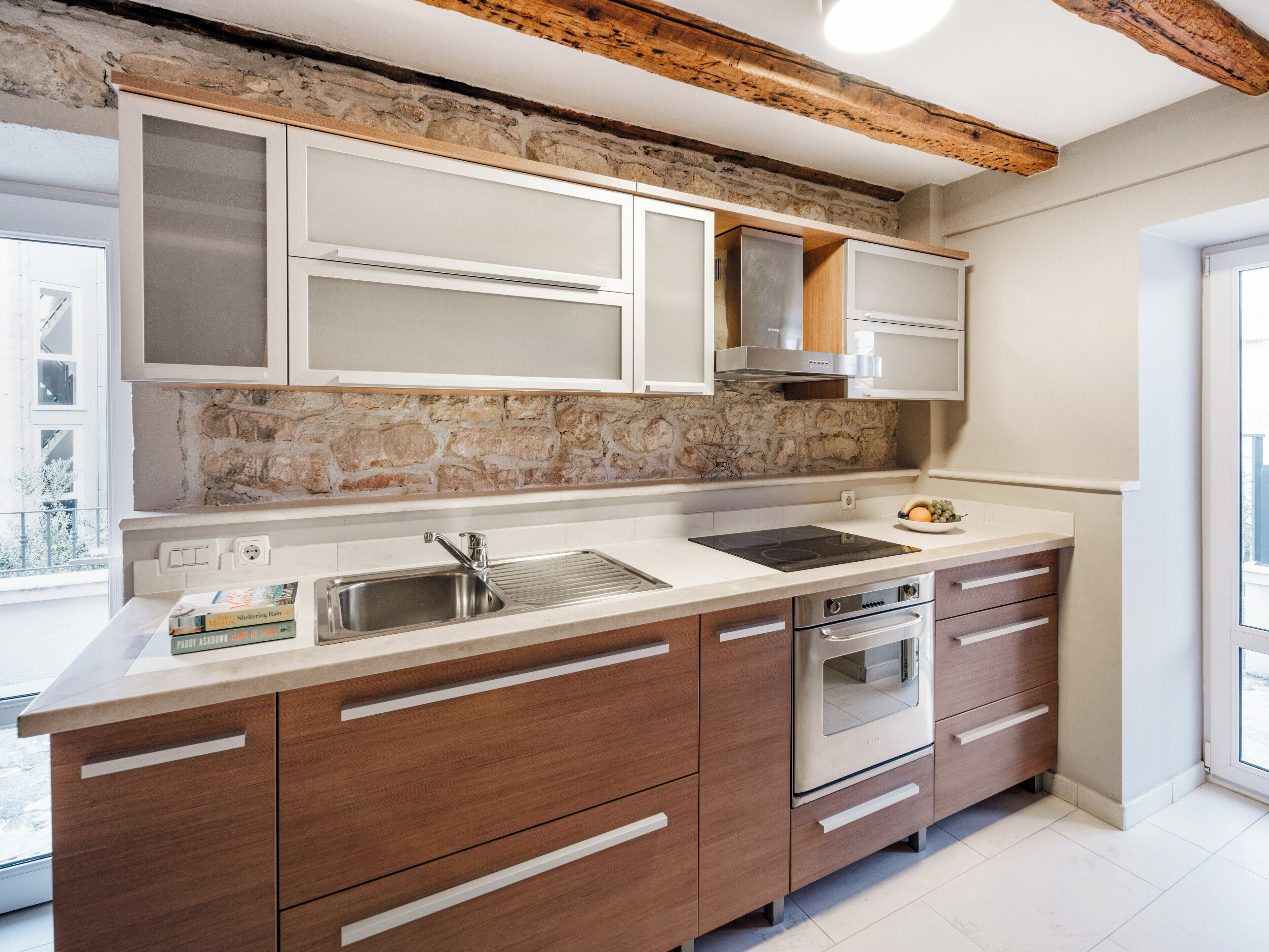 Una cocina moderna con armarios blancos, protector contra salpicaduras de piedra y vigas de madera.