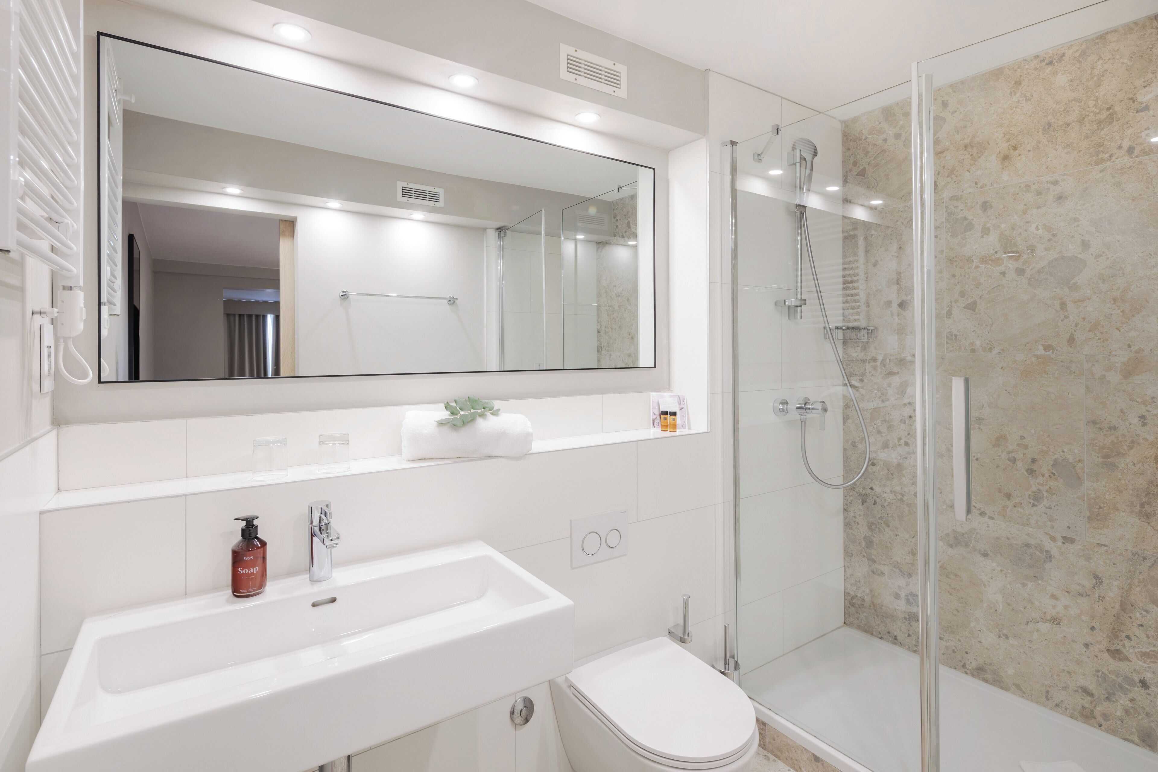 Une salle de bain moderne avec un grand miroir, un lavabo blanc et une douche à parois de verre.