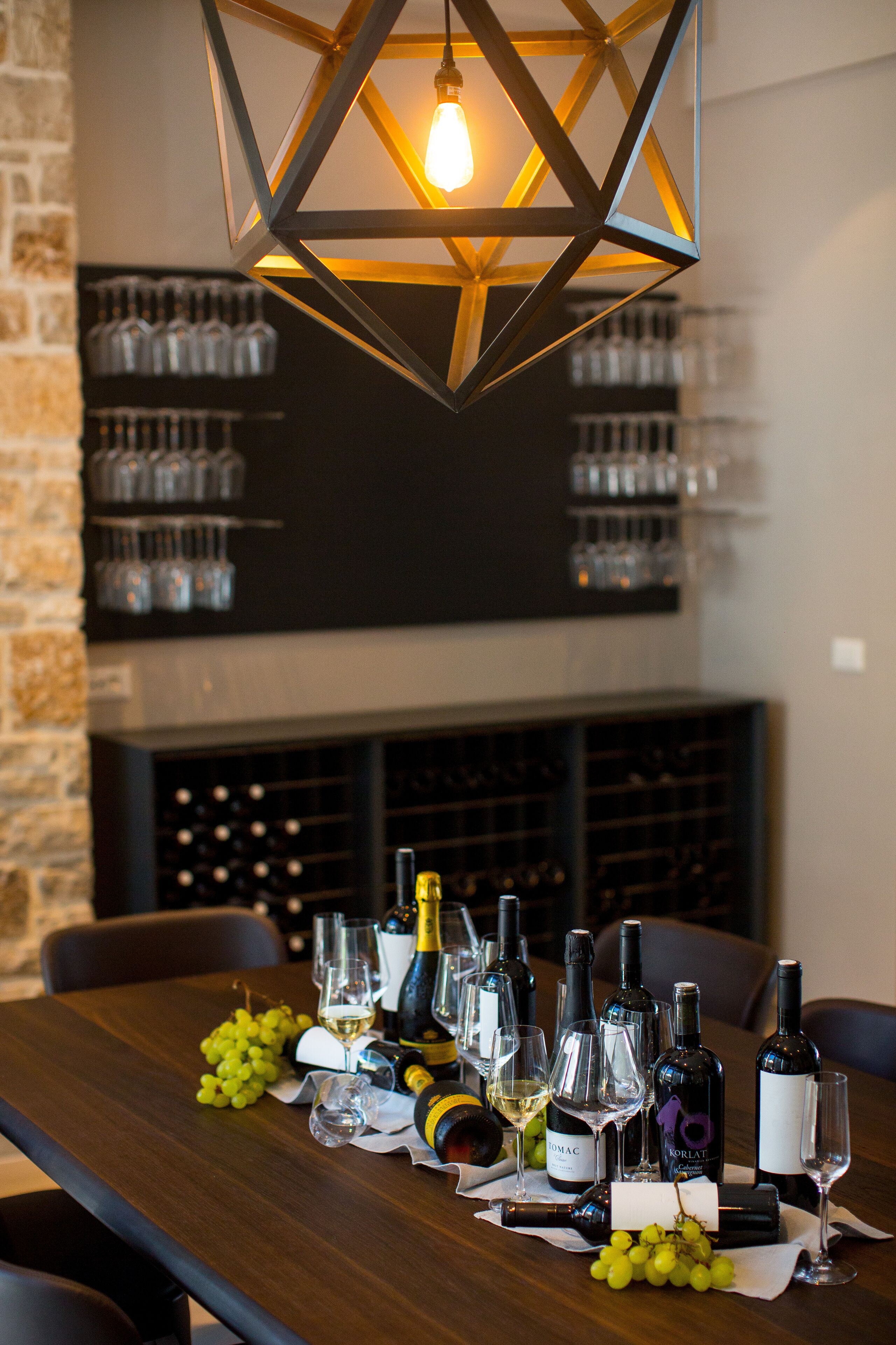 Una mesa de comedor preparada con botellas de vino, copas y uvas, con una botellera al fondo.