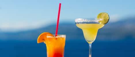 Two cocktails on a wooden table with a clear blue sky in the background.