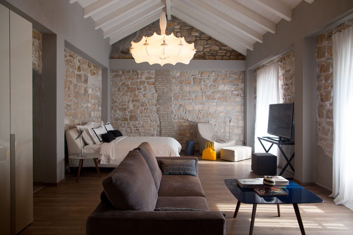 Una sala moderna con pared de piedra, una cama, un sofá, una mesa de centro y un televisor.