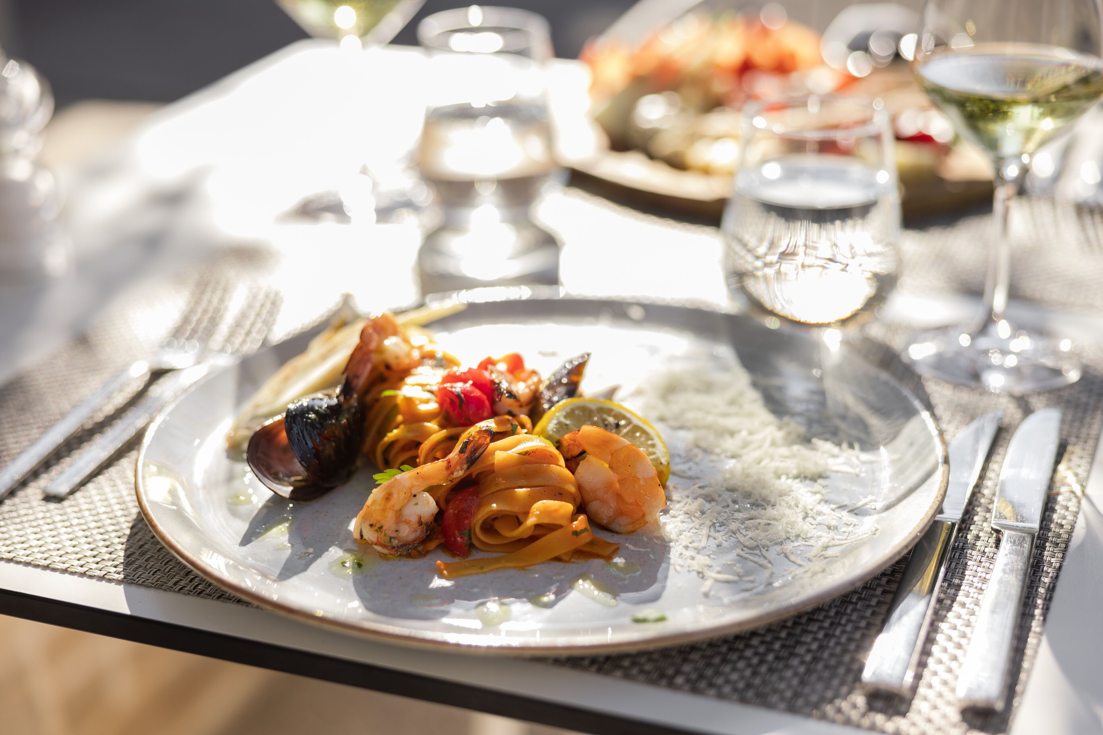A dining table with a plate of seafood pasta, a glass of water, and a glass of wine.
