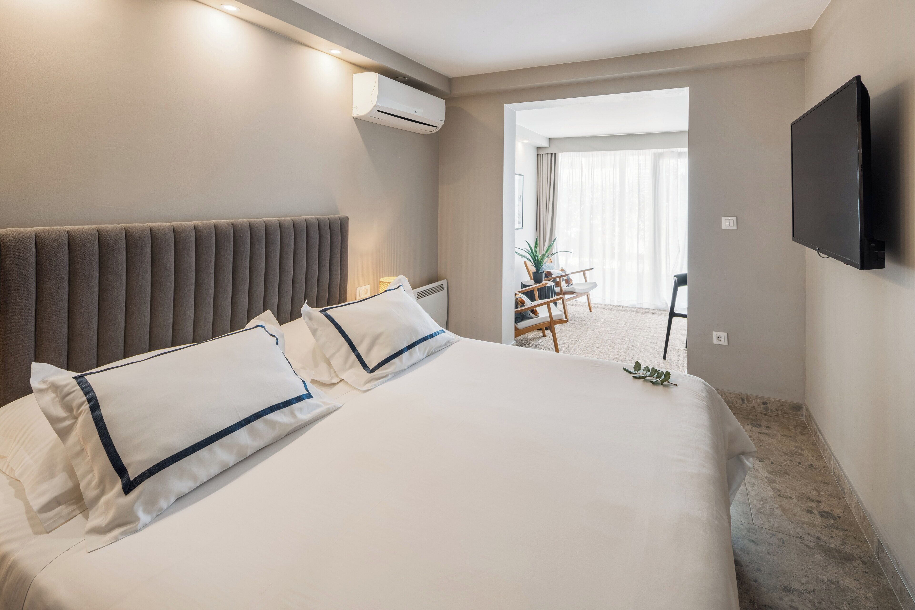 A modern hotel room with a large bed, a flat-screen TV mounted on the wall, and a view of the outdoor area.
