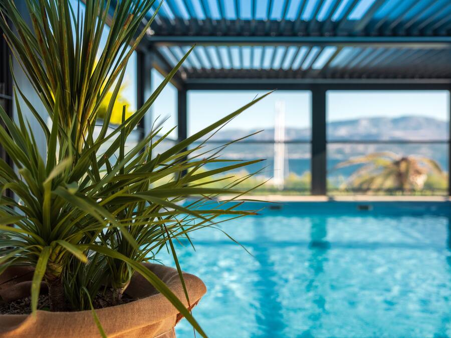A pool with a view of mountains, a potted plant, and a pergola structure.