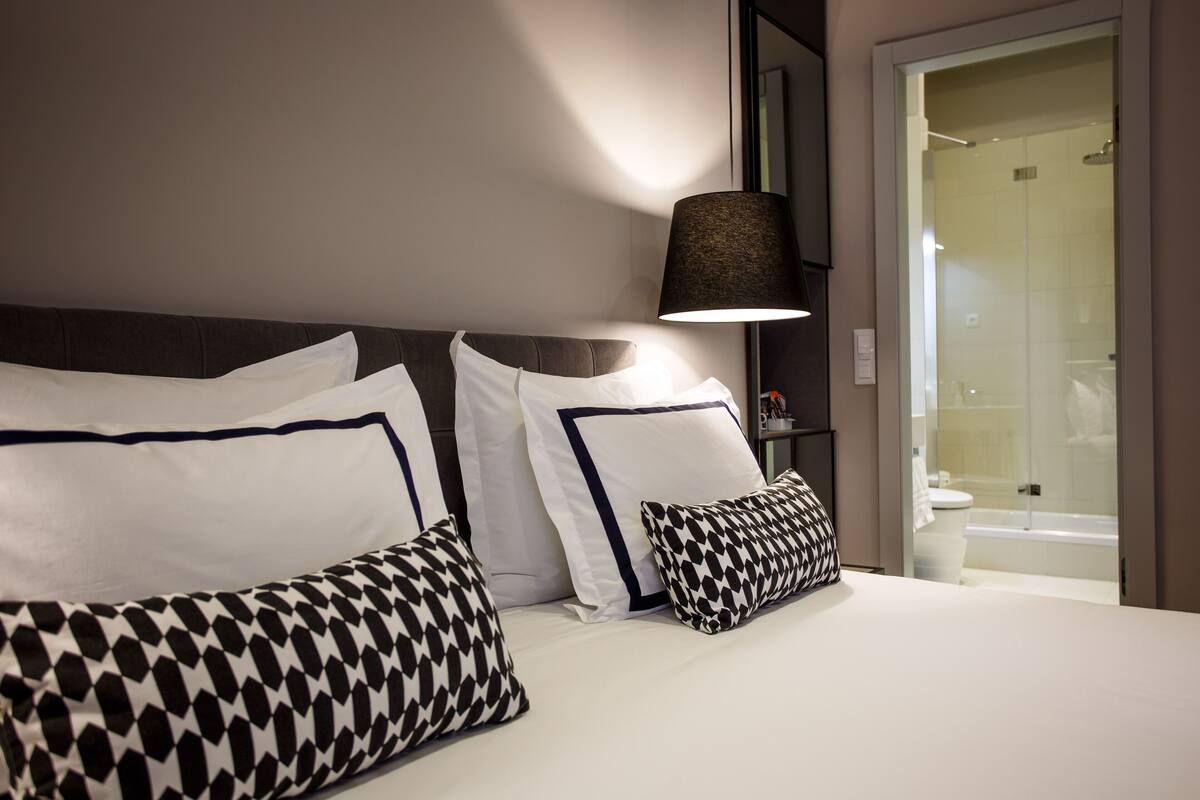 Una habitación de hotel con cama, ropa de cama blanca y un ventanal grande.