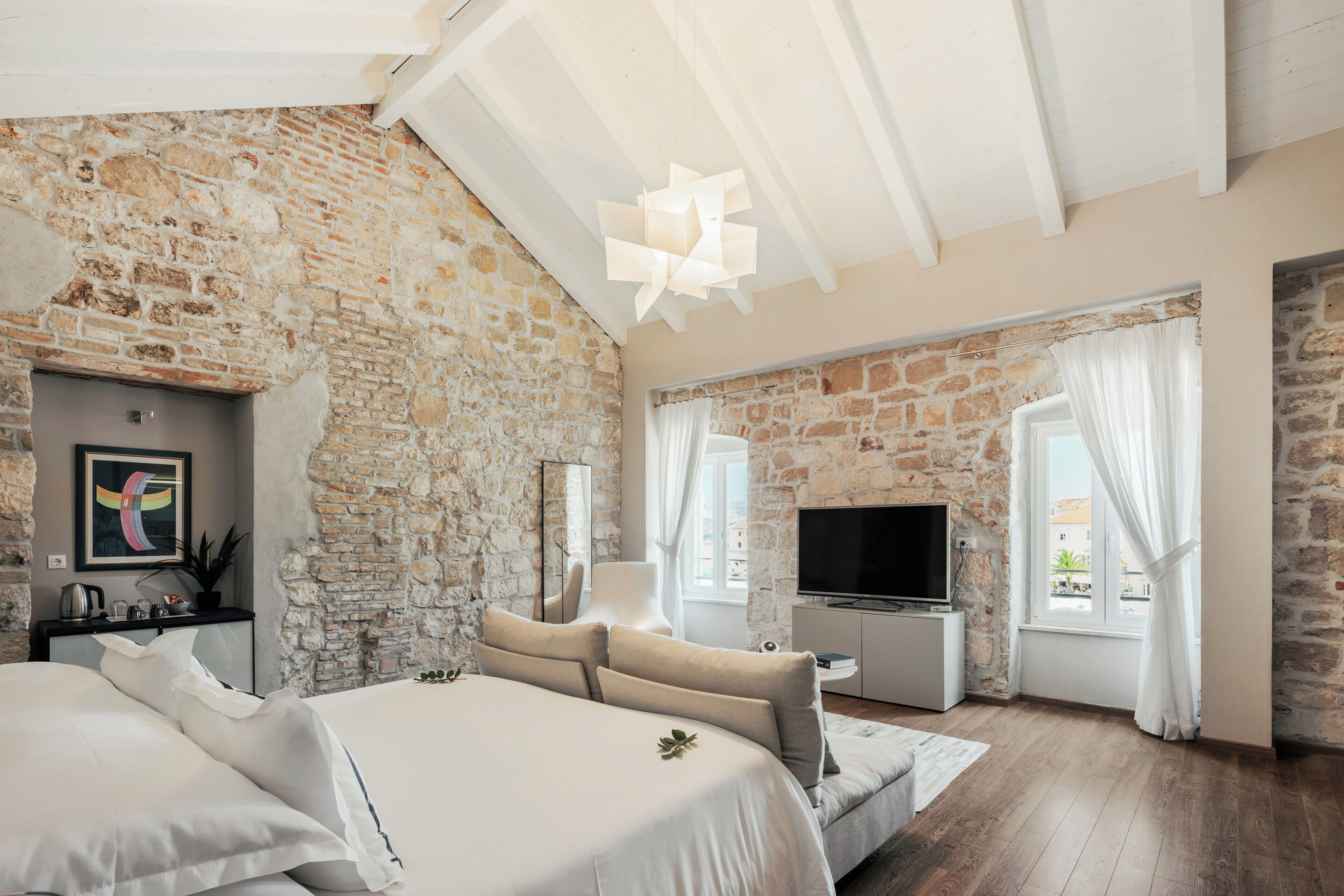 Ein Schlafzimmer mit Steinwand, einem Bett, einem Fernseher und einem Fenster mit Vorhängen.