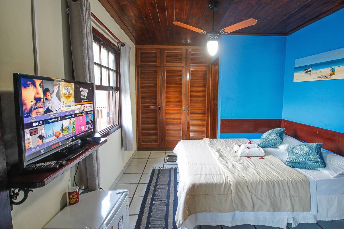 A bedroom with a bed, a television, a ceiling fan, and a wooden wardrobe.