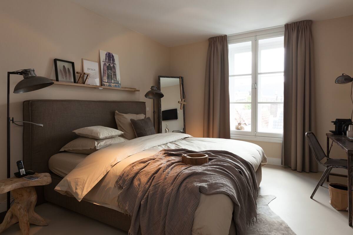 A bedroom with a bed, bedside table, lamp, and a window with curtains.