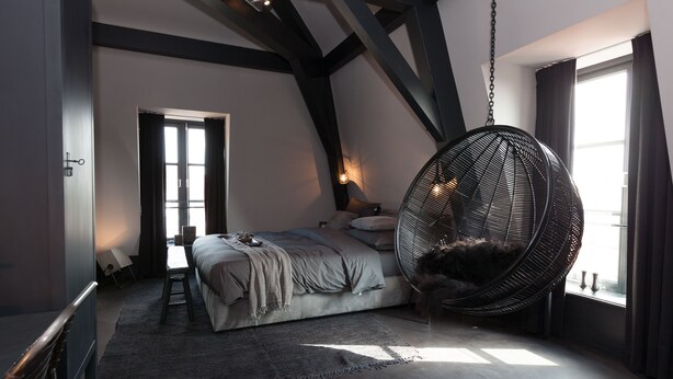 A bedroom with a large bed, a hanging chair, and a view of the outdoors. - Mother Goose Hotel (Utrecht)