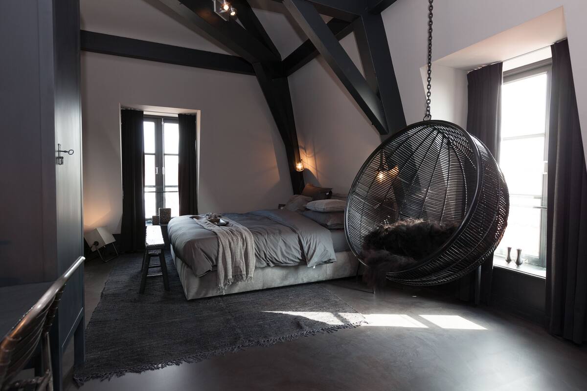A bedroom with a large bed, a hanging chair, and a view of the outdoors.