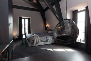 A bedroom with a large bed, a hanging chair, and a view of the outdoors. - Mother Goose Hotel (Utrecht)
