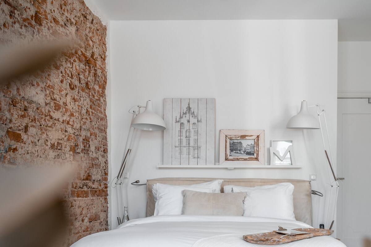 A bedroom with a large bed, white bedding, two bedside lamps, and a brick wall.