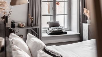 A bedroom with a large bed, a window seat with a view, a desk with a lamp, and a nightstand with a lamp.