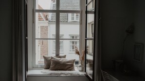 A room with a window seat featuring a white furry rug, two pillows, and a vase with dried pampas grass. - Mother Goose Hotel (Utrecht)