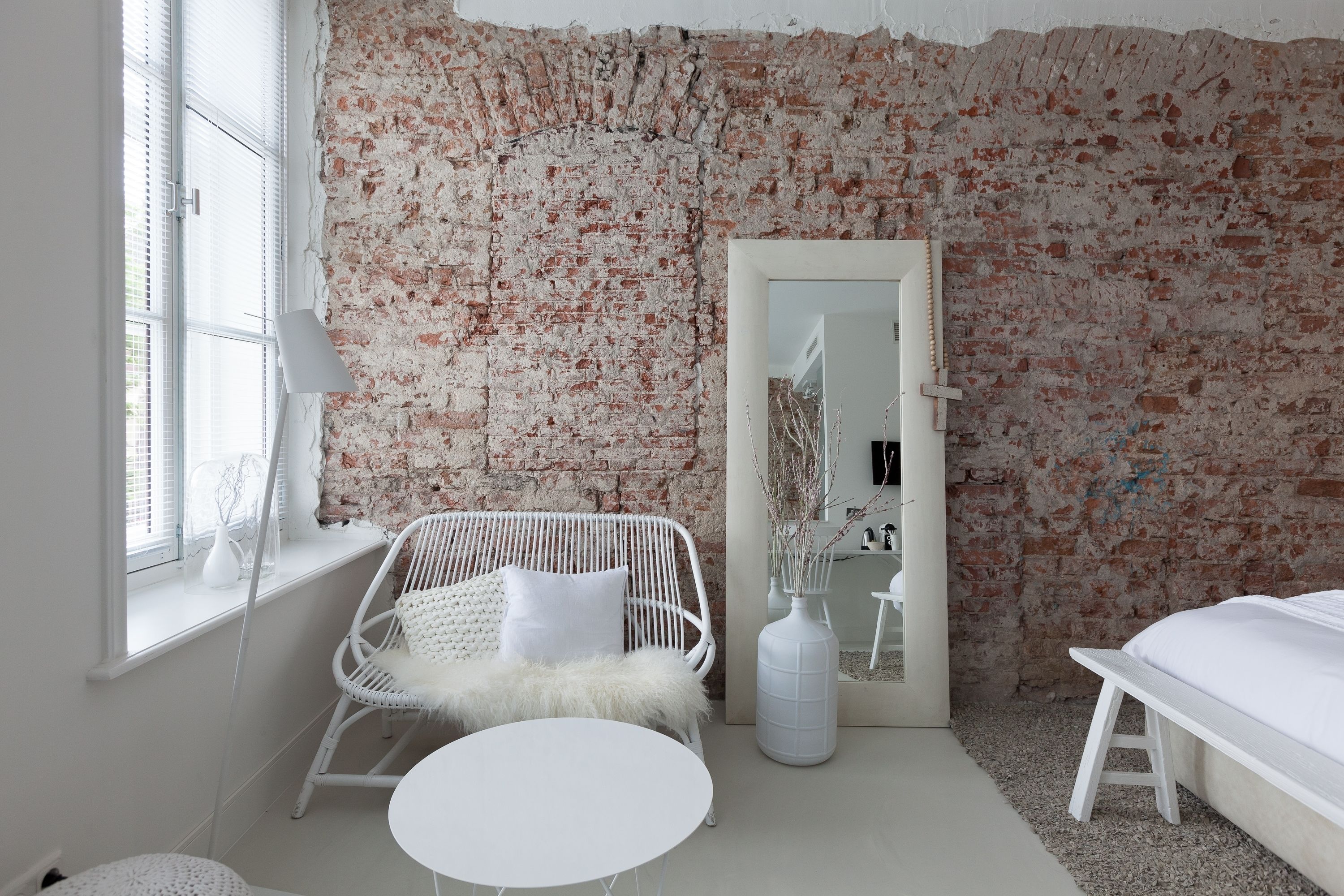 A room with a brick wall, a white wicker chair, a round table, and a bed.