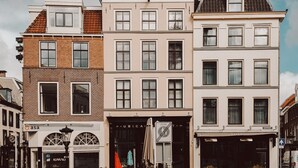 A row of three-story buildings with a mix of brick and white facades, a bicycle parked in front, and a clear blue sky with clouds. - Mother Goose Hotel (Utrecht)