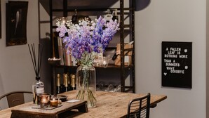 A wooden dining table with chairs, a vase of flowers, and a candle on a shelf. - Mother Goose Hotel (Utrecht)