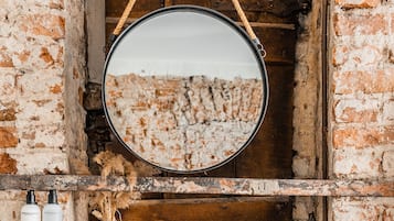 A rustic bathroom with a wooden shelf, a hanging mirror, and a white sink.