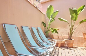 A row of blue lounge chairs and a small table on a wooden deck with potted plants. - Latroupe Poblenou Beach (Barcelona)
