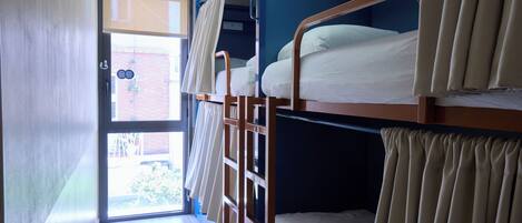 A dormitory-style room with bunk beds, a window, and a door leading outside.