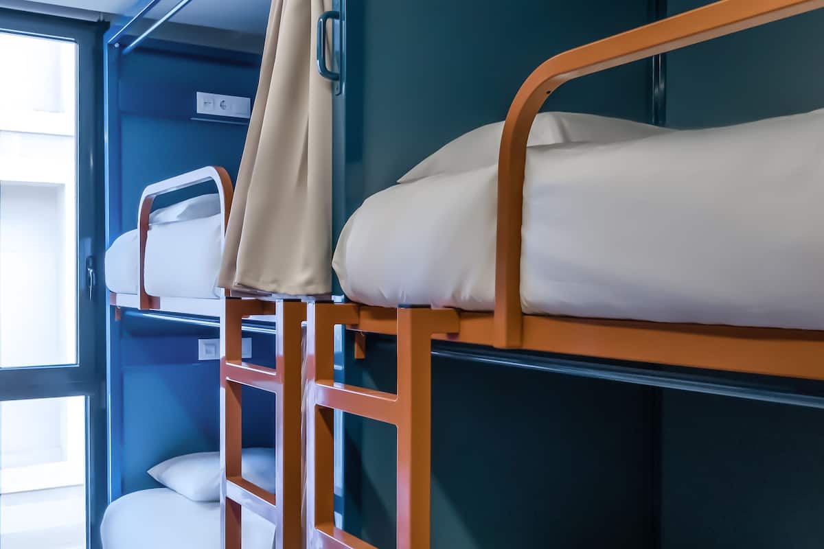 A bunk bed room with a window, wooden ladder, and a blue wall.