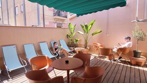 A terrace with lounge chairs, a table, and potted plants.