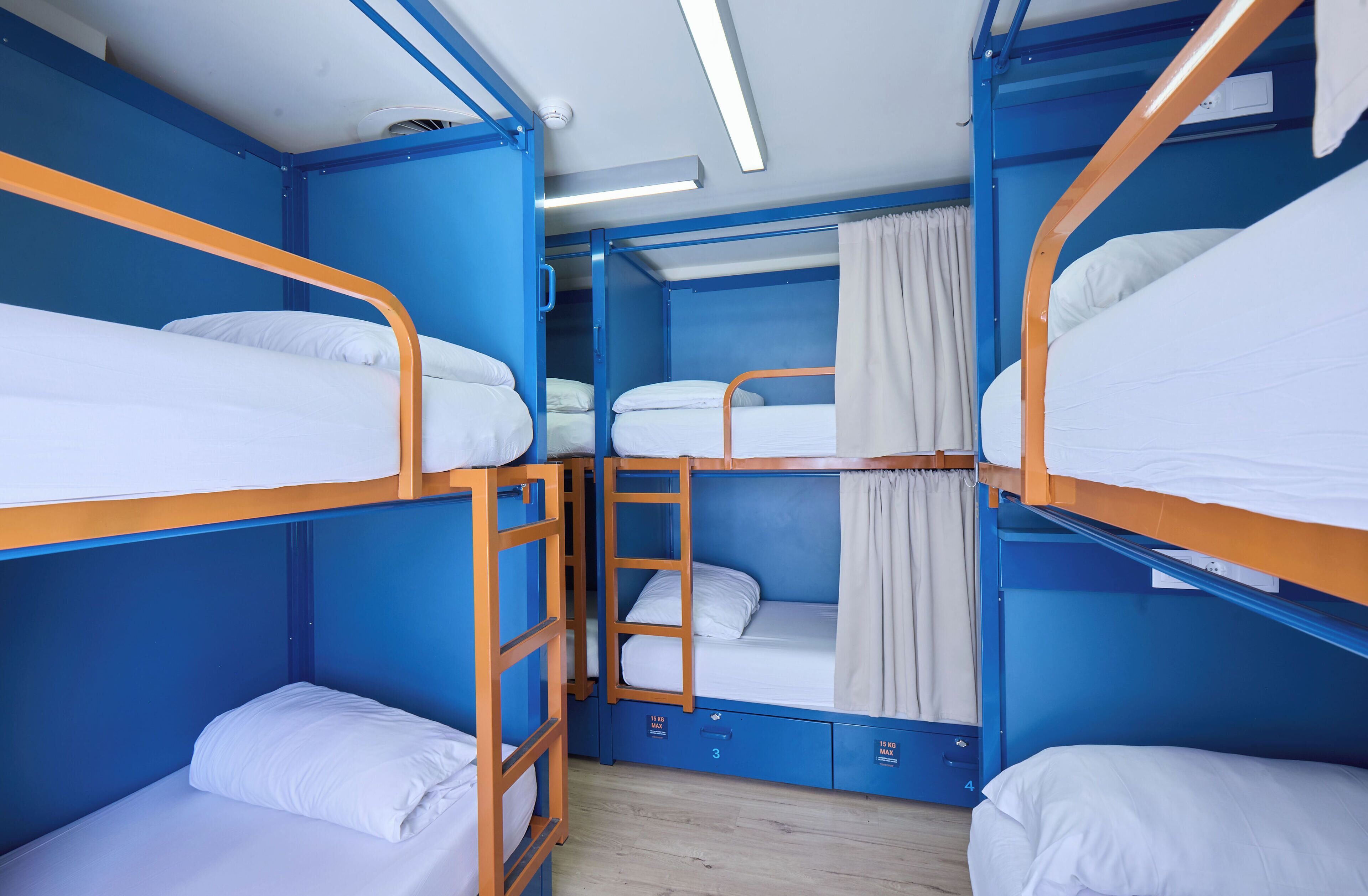 Habitación con literas, paredes azules, ropa de cama blanca y una escalera de madera.