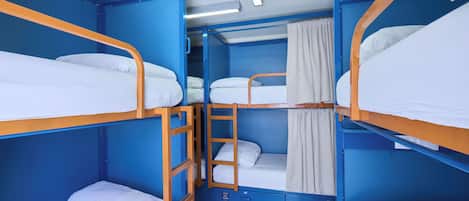 Habitación con literas, paredes azules, ropa de cama blanca y una escalera de madera.