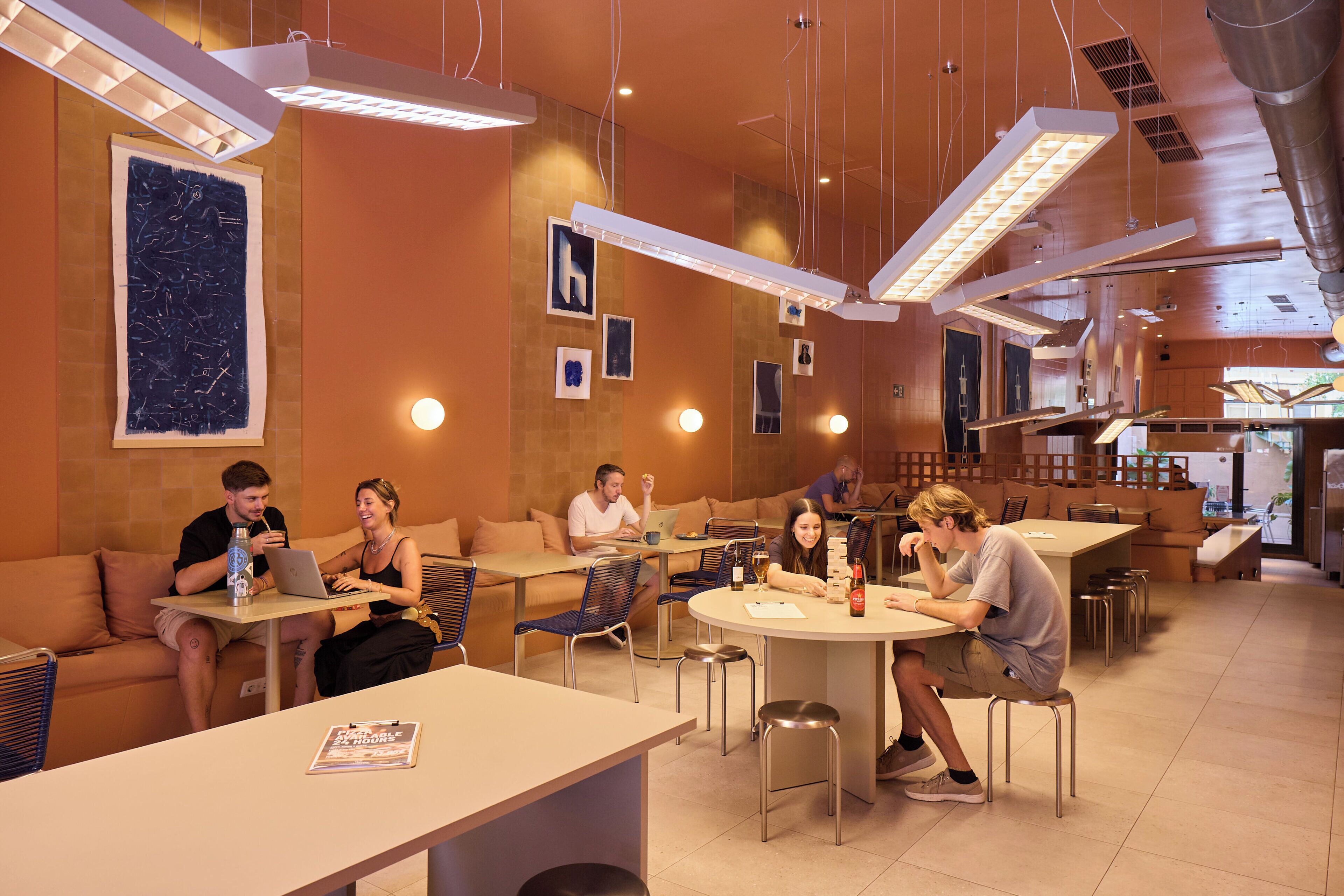 A modern cafe with multiple seating areas, including tables and a couch, with overhead lighting and artwork on the walls.