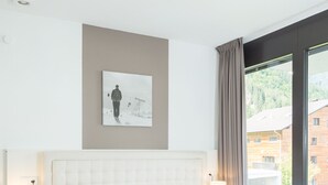 Une chambre d’hôtel avec un grand lit, une table de chevet avec une lampe, un tableau au mur et une fenêtre donnant sur des immeubles.