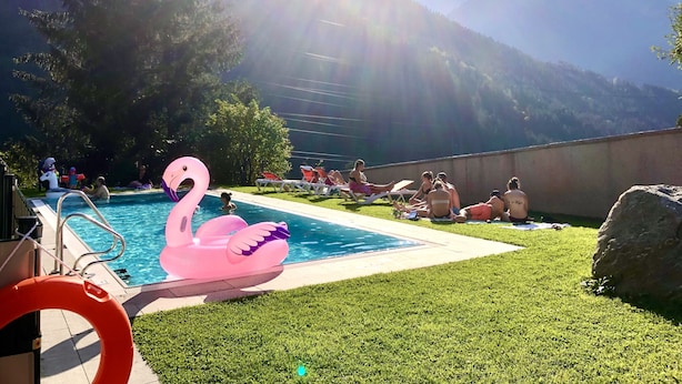 Une piscine agrémentée d’un flotteur en forme de flamant rose, entourée d’une pelouse et avec une chaîne de montagnes en toile de fond.