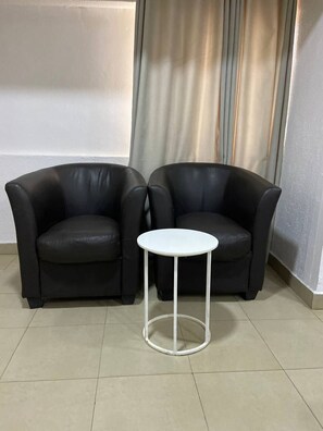 Two black leather armchairs and a small white table in a room with tiled flooring and a curtain. - Solitude Hotel Yaba (Lagos)