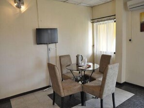 A small, round glass table with four chairs, a flat-screen TV mounted on the wall, and a window with curtains. - Solitude Hotel Yaba (Lagos)