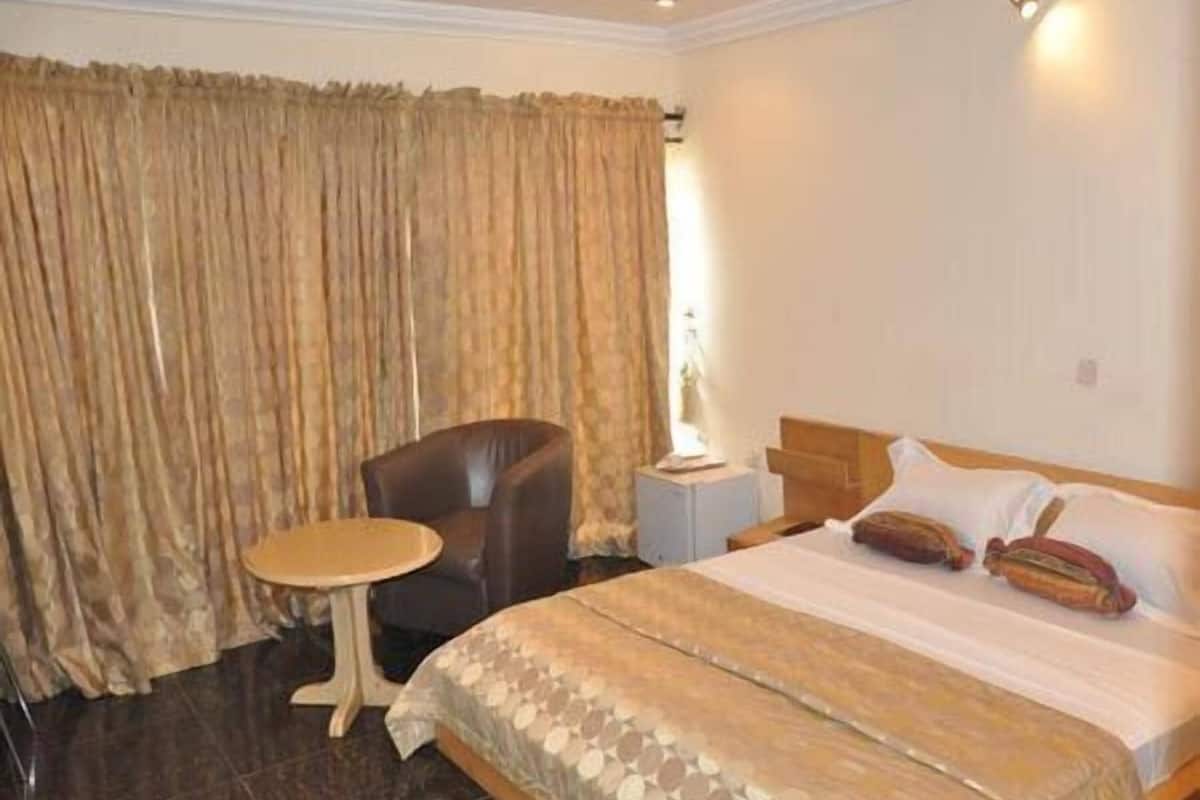 Une chambre d’hôtel avec un lit, une chaise, une petite table et des rideaux.