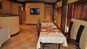 Ein Essbereich mit einem langen Tisch, der für eine Mahlzeit gedeckt ist, Stühle, einem Fernseher an der Wand und einer Wanduhr.