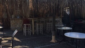 An outdoor seating area with thatched umbrellas, stone walls, and a stone bench. - Ilena Hotel (Corfu)