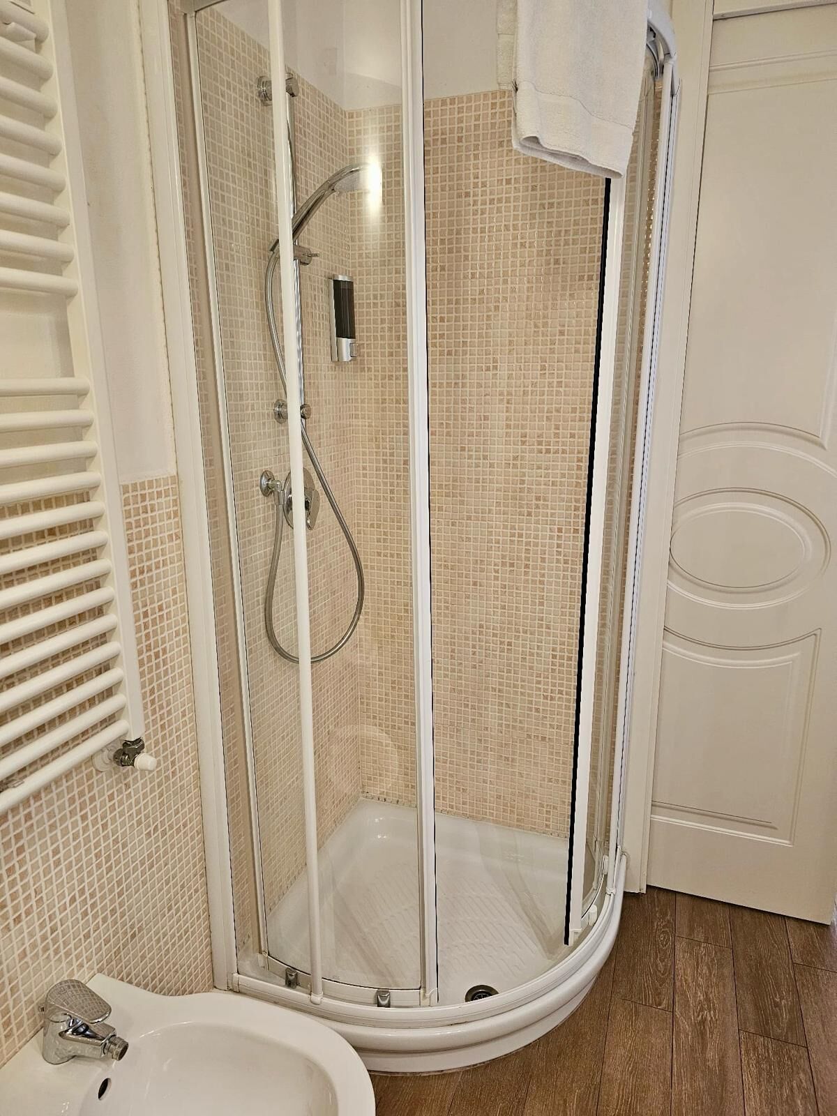 A shower with a glass door, a white sink, and a wooden floor.