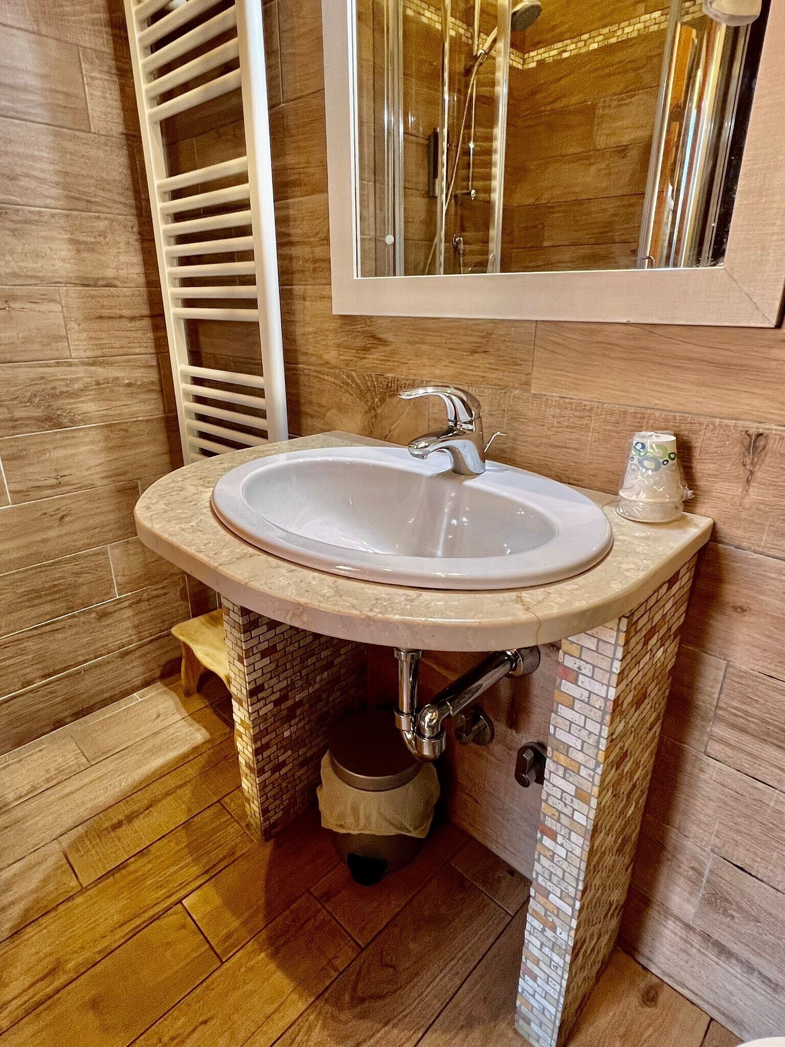 A bathroom with a white sink, a mirror above it, and wooden flooring.