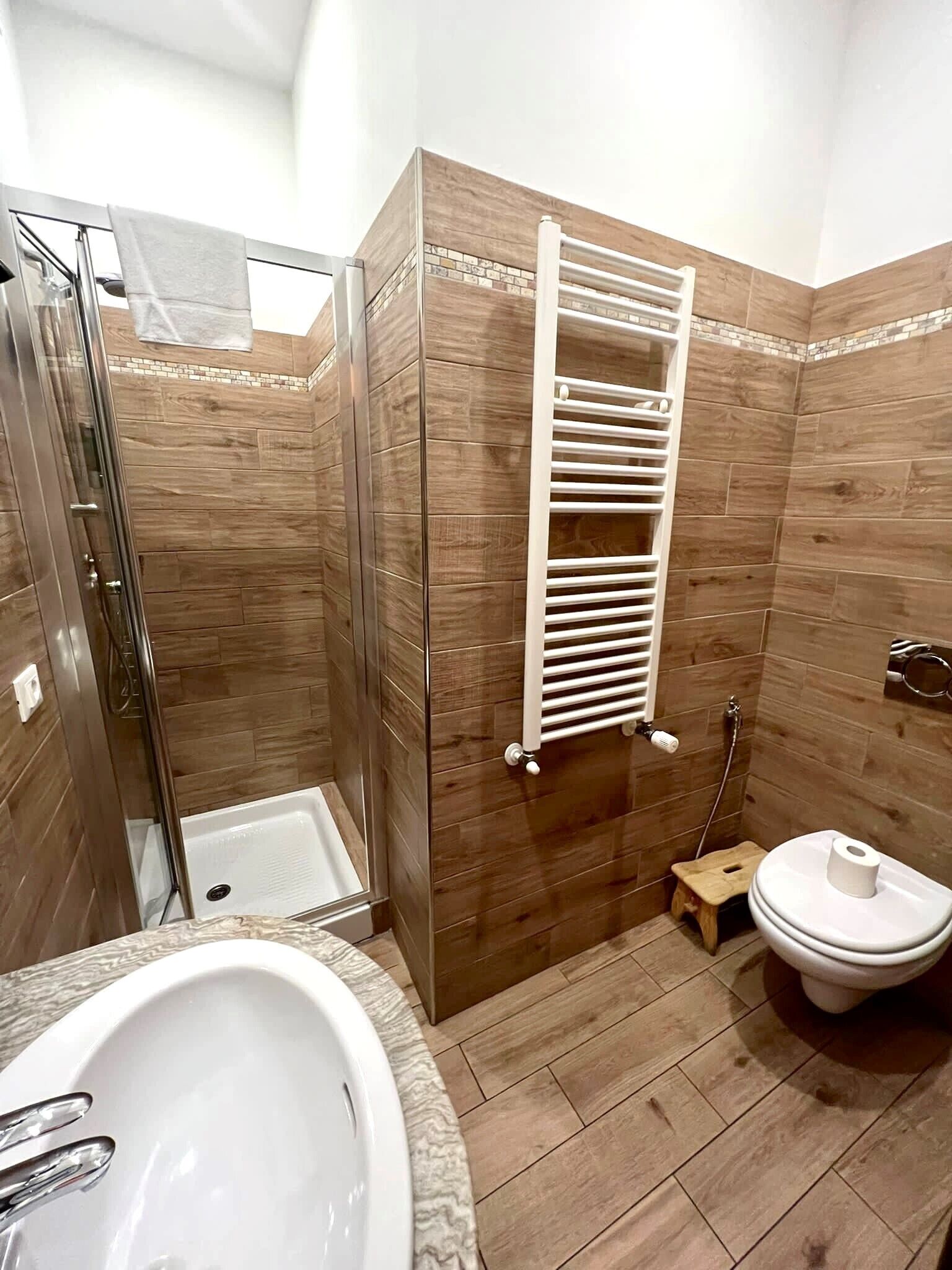 Un baño con cabina de ducha de vidrio, una bañera blanca, un inodoro blanco y un taburete de madera.