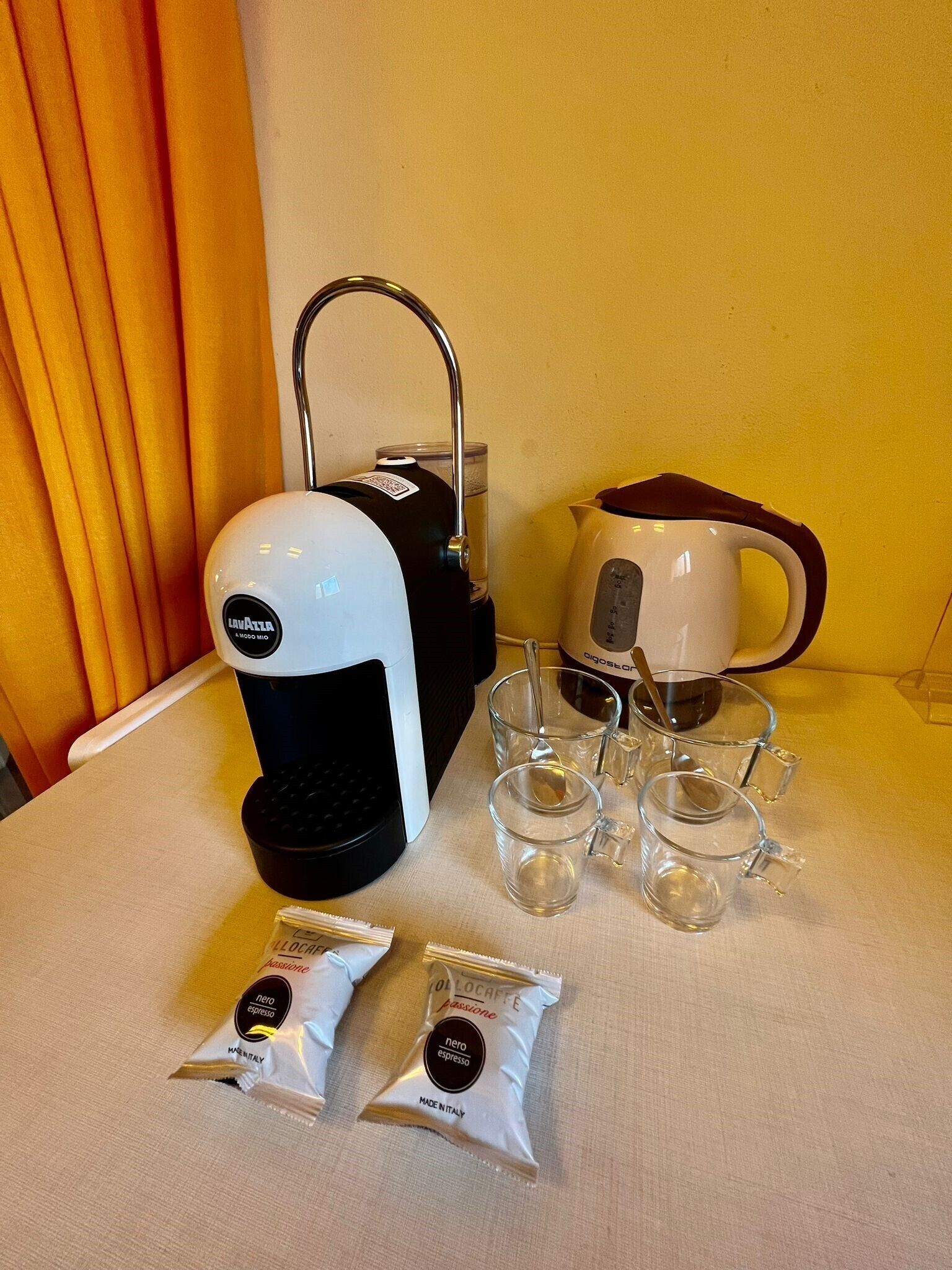 A coffee maker, a kettle, and two packets of coffee on a table.