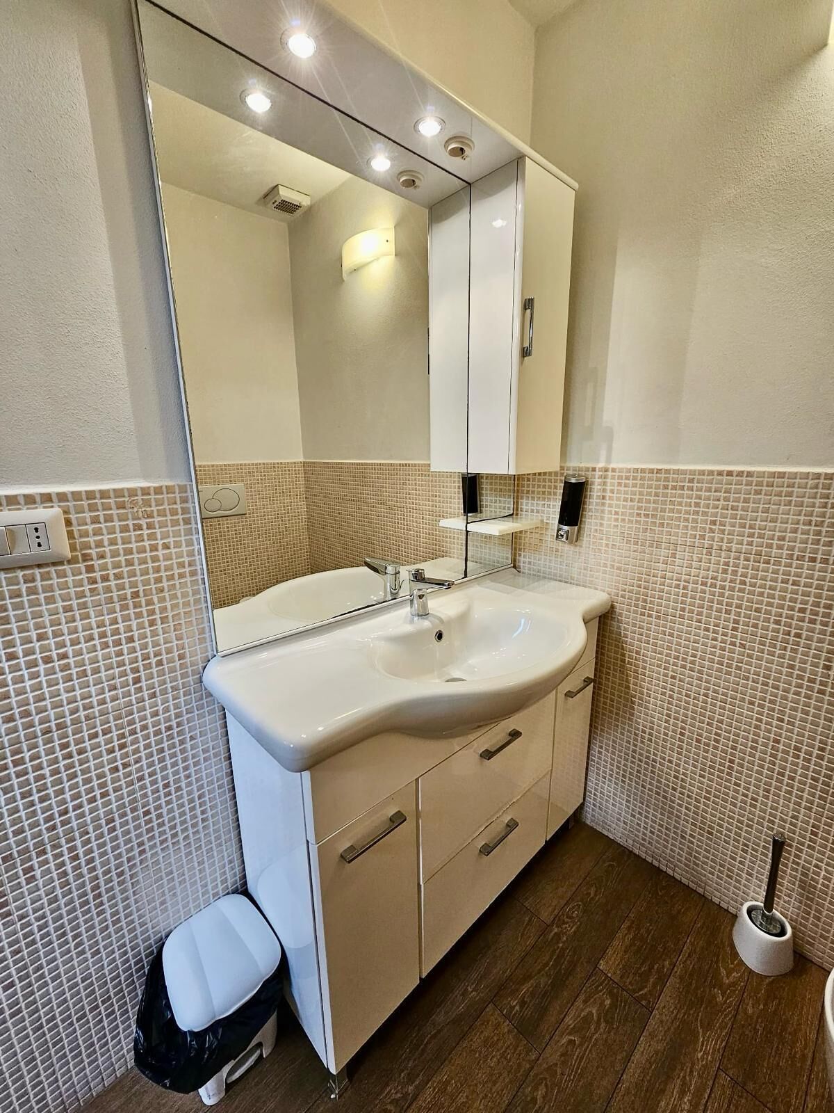Un baño con lavamanos blanco, armarios color beige, un espejo y un salpicadero de azulejos.