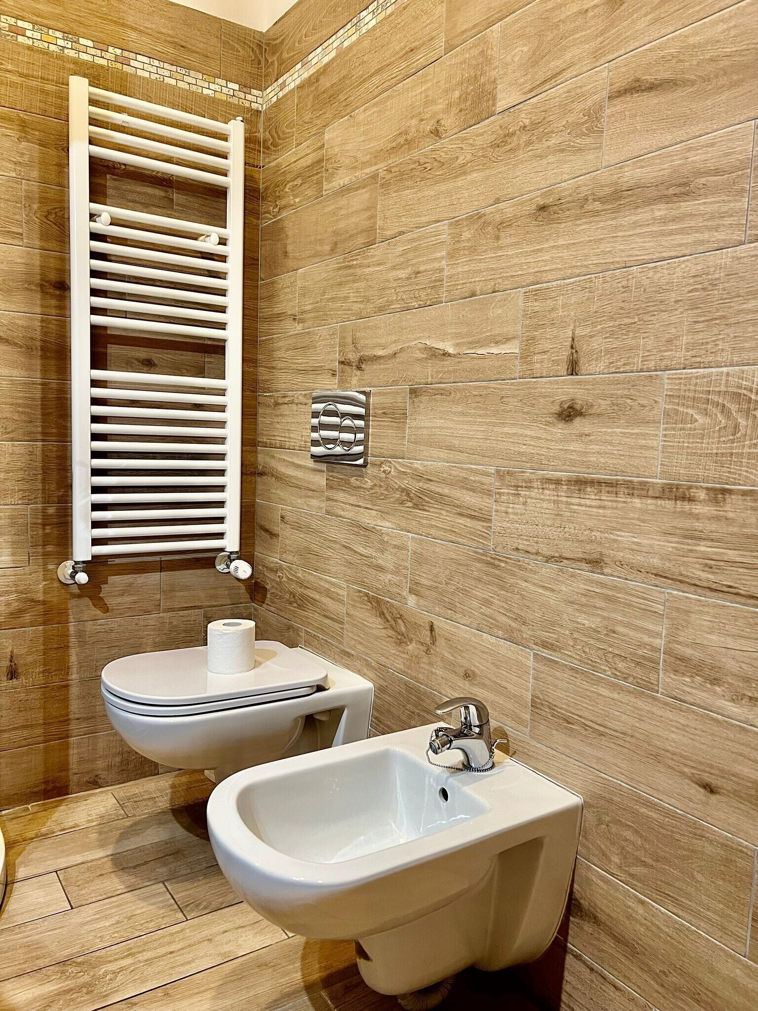 A bathroom with a wooden wall, a white towel rack, a bidet, and a sink.