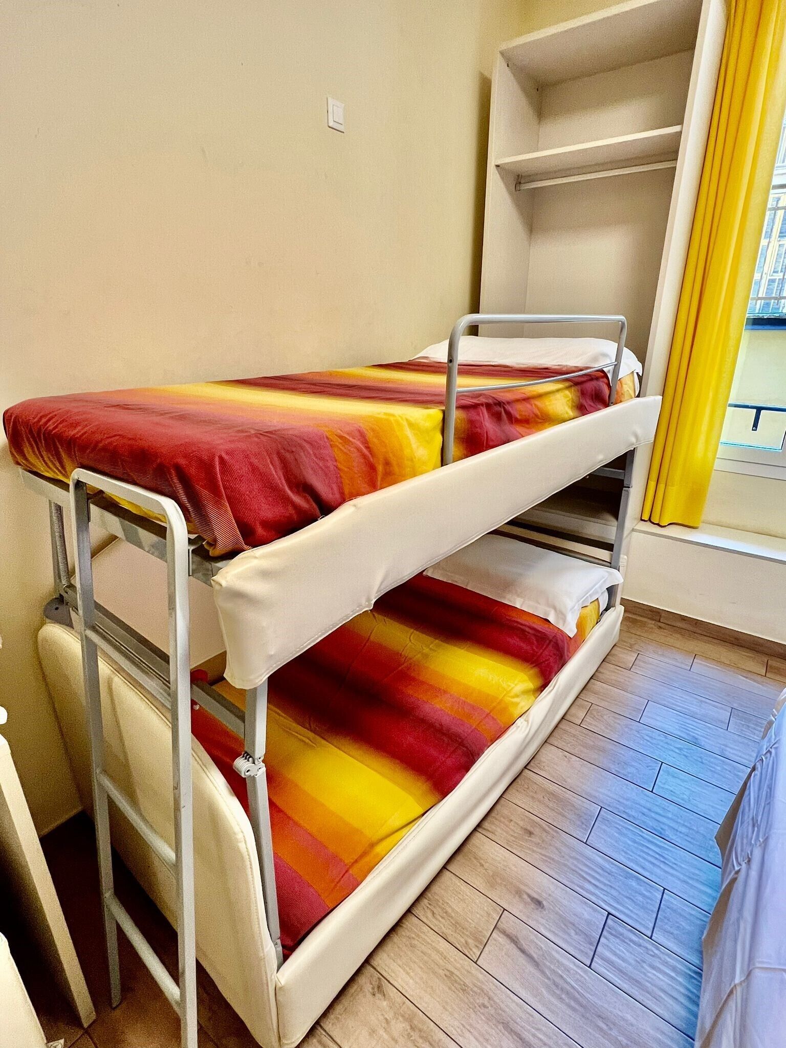 A bunk bed with a colorful blanket, a metal ladder, and a wooden floor.