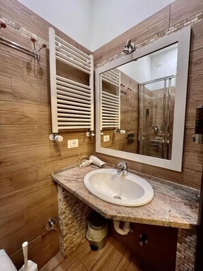 A modern bathroom with a granite countertop sink, a large mirror, and wooden paneling. - Casa Zeffirino (Sanremo)