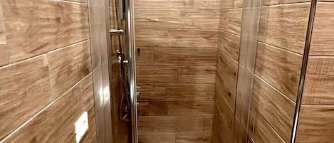 Un área de ducha pequeña y cerrada con puerta de vidrio, paredes de madera y suelo blanco.