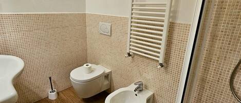 Un baño con inodoro, bidé y asiento de bidé, ducha con puerta de cristal y un perchero para toallas.