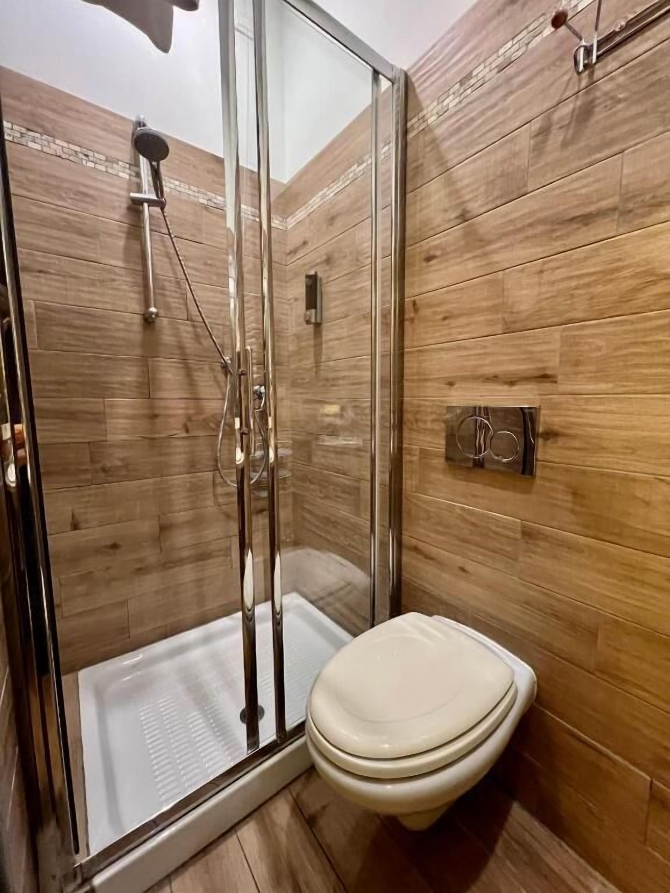 A modern bathroom with a glass-enclosed shower, a toilet, and wooden paneling on the walls.